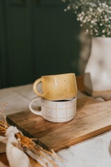 Two yellow and white coffee mugs sit on a wooden board. The mugs are placed next to each other, and...