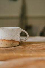 A white mug with a brown handle sits on a wooden table. The mug is empty and the table is made of wood