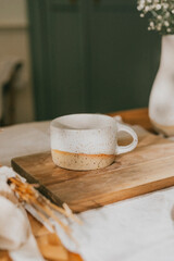 A white and yellow mug sits on a wooden cutting board. The mug is decorated with a pattern of yellow and white dots. The scene is simple and uncluttered, with the focus on the mug