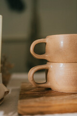 Two cups with handles sit on a wooden table. The cups are brown and appear to be made of ceramic....