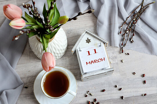 Calendar for March 11: numbers 11, name of the month March in English on a decorative calendar, cup, bouquet of tulips