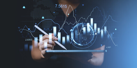 Digital financial analysis concept with hand using stylus on tablet and glowing graphs on blue...