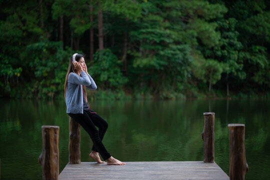 Woman listens to music via Bluetooth headphones, enjoying the peaceful lakeside view