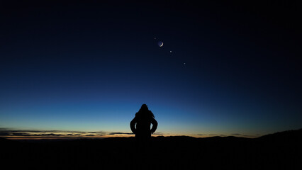 Silhouette of a woman observing Moon, planets and Milky Way stars from a dark countryside location.