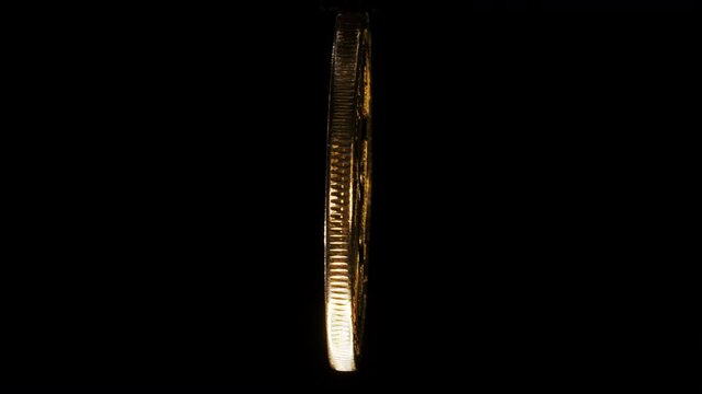Physical golden plated coin with the Bitcoin logo spins around its axis on black background.