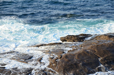 Close-up of waves crashing against rugged coastal rocks, creating a striking contrast of blue water and white foam, showcasing the dynamic power of the Atlantic Ocean
