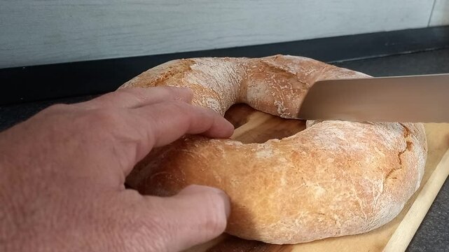 Video in cui si vede la mano di un uomo che taglia un pezzo di pane a forma di ciambella 