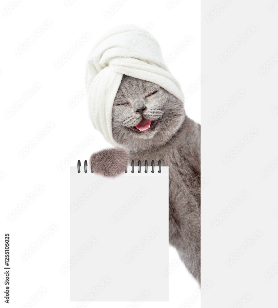 Leinwandbilder Happy cat with towel on it head looks behind blank white banner and shows blank notebook. Empty space for text. Isolated on white background