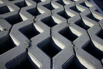 Fototapeta premium Close-up view of interlocking concrete paving blocks arranged in a zigzag pattern. The geometric design creates strong shadows and depth, highlighting the texture and structure of the material