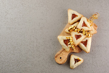 Close up freshly baked triangular cookies filled with fruit surrounded by golden decorations ribbon on a wooden cutting board. Purim celebration concept. top view