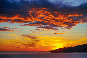 View of horizon over ocean in the distance there are islands and mountains with orange tinted clouds texture before sunrise early in the morning