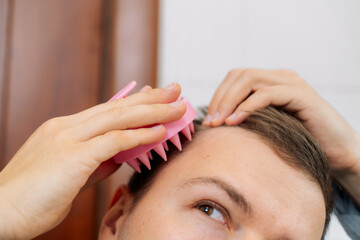 Naklejka premium Young man using hair scalp massager, closeup