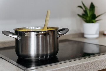 A stainless steel pot with soup and a wooden spoon placed on an induction stove in a modern...
