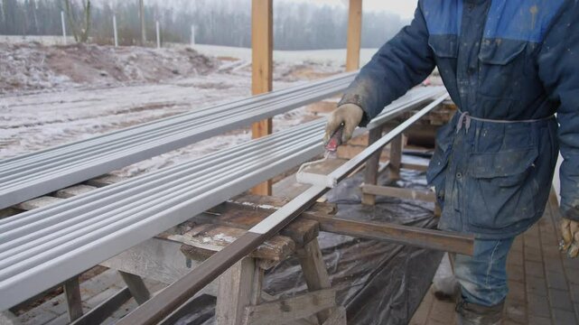 A dedicated worker skillfully handles metal sheets in a snowy construction area, showcasing winter building activities