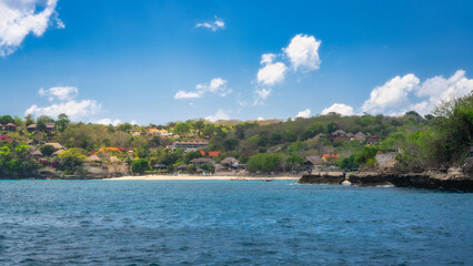 Naklejka premium Discover a breathtaking view of a tropical coastline with vibrant greenery, turquoise waters, and a sandy beach under a bright blue sky, ideal for a serene vacation, Nusa Lembongan, Bali, Indonesia