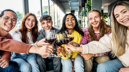 Multiracial group of friends toasting red wine sitting at bar restaurant table - Millennial people enjoying dinner party together - Life style concept with guys and girls hanging out on weekend