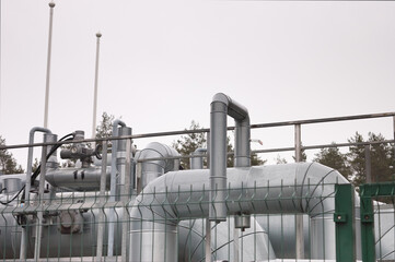 pipeline and pipeline elements behind metal fence and mesh against gray sky