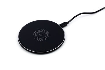 Black round charging pad and connected power cord isolated on white background. Modern technologies...