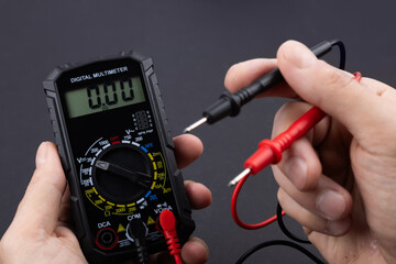 Hand holding a digital multimeter with test leads, on a dark background © eliosdnepr