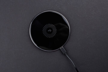 Black round charging pad and connected power cord on dark background. Modern technologies concept