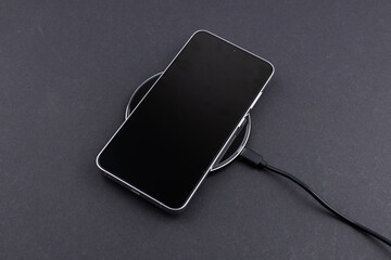 Mobile smart phone on wireless charging device on dark background. smartphones connected to power...