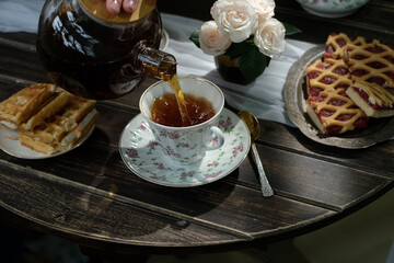Afternoon tea. Pouring brewed black tea from teapot into cup. 