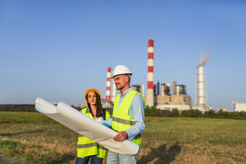 Engineers holding blueprint discussing project near power plant