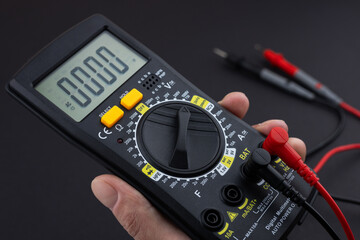 Hand holding a digital multimeter with test leads, on a dark background