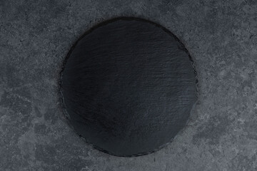 Round rustic black slate stone plate, on stone background