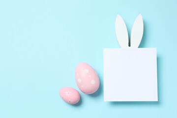 Happy Easter. Colorful eggs, white paper card and Easter bunny ears on a pastel color background,...