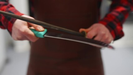 A man is holding a pair of scissors and a knife. The scissors are green and the knife is brown. The man is wearing an apron