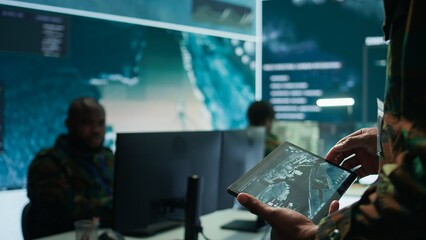 Military officer leads cybersecurity operations in a high tech operation room command post,...