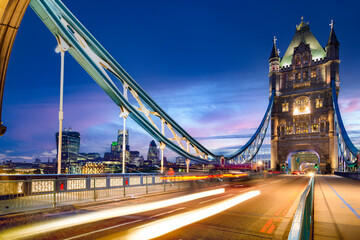 London’s iconic Tower Bridge illuminated at dusk, with light trails from passing vehicles and the modern city skyline in the background