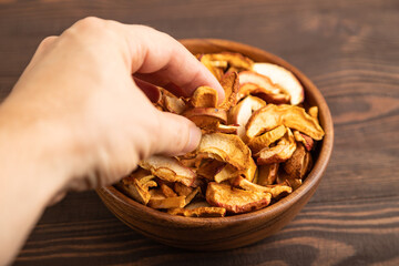 Dried Apples in wooden bowl with hand on brown wooden. Side view, close up, selective focus