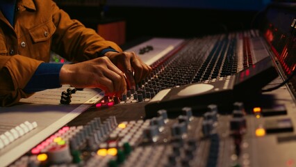African american producer uses control desk with automatic equalizer, mixer and sliders to edit...