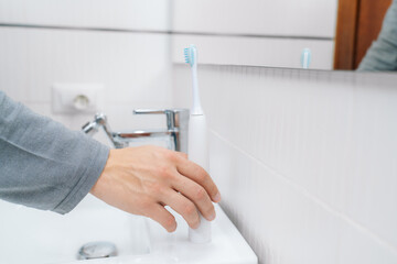 A modern electric toothbrush in white colour stands on the edge of the bathroom sink.