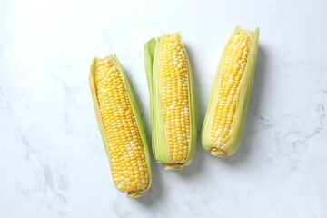 Fresh corn on cobs on marble background, top view