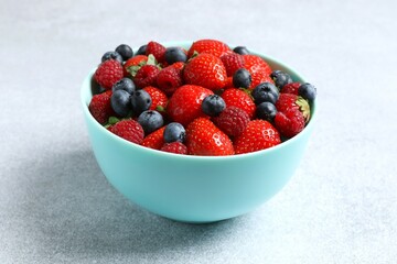 Different fresh ripe berries in bowl on gray table