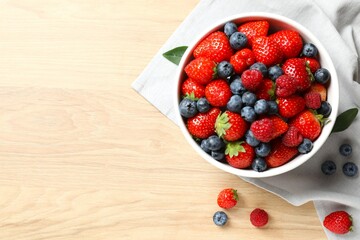 Different fresh ripe berries in bowl on wooden table, top view