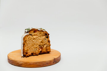 A sliced Easter cake with white icing, decorated with green leaves, served on a white plate, revealing its soft texture with dried fruits, alongside vibrant yellow eggs for a festive presentation.