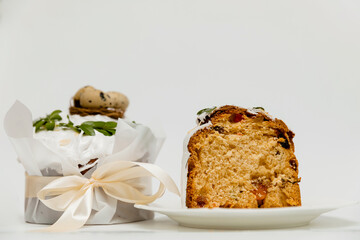 A festive Easter cake with white icing, decorated with green leaves, next to two vibrant yellow eggs and a wooden board, with a cut slice revealing a soft, fluffy texture with dried fruits inside.