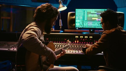Artist songwriter recording a new track on his electro acoustic guitar in professional studio,...