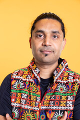 Portrait of optimistic indian man wearing colorful vest with positive facial expression smiling, looking pleased. Calm person in traditional clothing, feeling satisfied, studio backdrop, close up shot