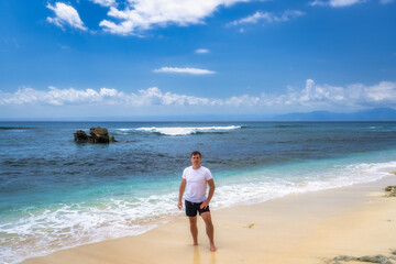 A man stands on a beautiful and picturesque beach, fully enjoying the warm sun and gentle waves, with clear blue skies and crystalclear water visible in the background, Nusa Lembongan, Bali, Indonesia