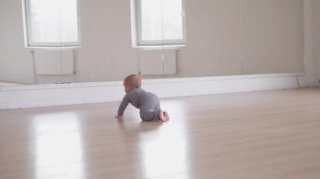 In a spacious, welllit room filled with sunlight, a cute little baby is happily crawling across the soft, wooden floor
