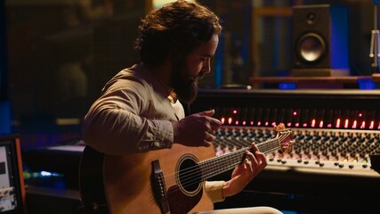 Young artist songwriter composing a new song on guitar in recording session at studio, creating...