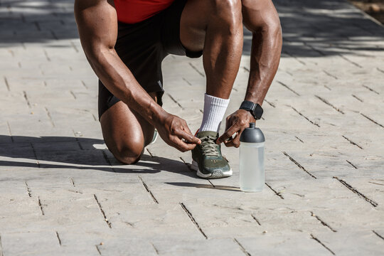 African-American man ties shoelaces before playing sports in a public park on a sunny day