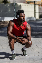 Man performs squats in a park while listening to music with headphones on a sunny day