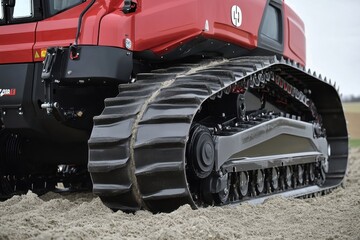 Close-Up View of Red Agricultural Machine Tread on Sandy Terrain