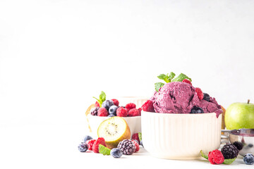 Homemade fruit and berry sorbet ice cream, portioned bowl with healthy fruit and berry yogurt gelato with fresh blueberry, raspberry, strawberry, blackberry, apples, kiwi on kitchen table